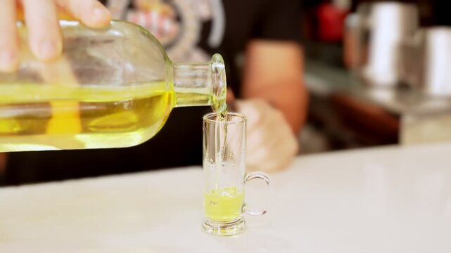 Bartender pouring yellow limoncello liqueur into shot glass