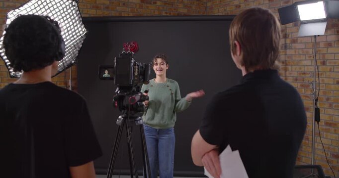 Production team cueing presenter delivering lines and gesturing in studio with handheld mic, tripod