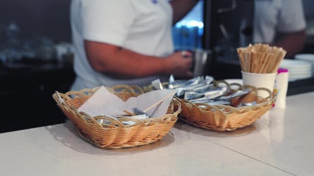 Conference catering service with wicker baskets, disposable cutlery and wooden skewers on a buffet counter, with a food service worker in the background