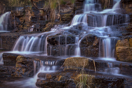 View of Fortescue Falls cascading over dark, layered rock formations in Karijini, Western Australia, Australia.