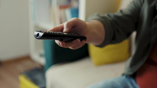 Hand detail of adult man operating infrared wireless remote control on sofa