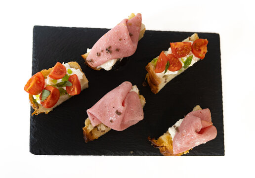 Top view of focaccia crostini with mortadella, stracciatella cheese and cherry tomatoes on black slate, Italian appetizer