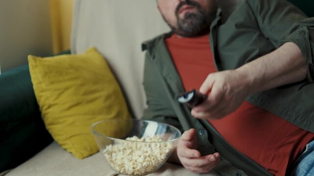 Casual man lying on sofa eating popcorn and looking around in living room