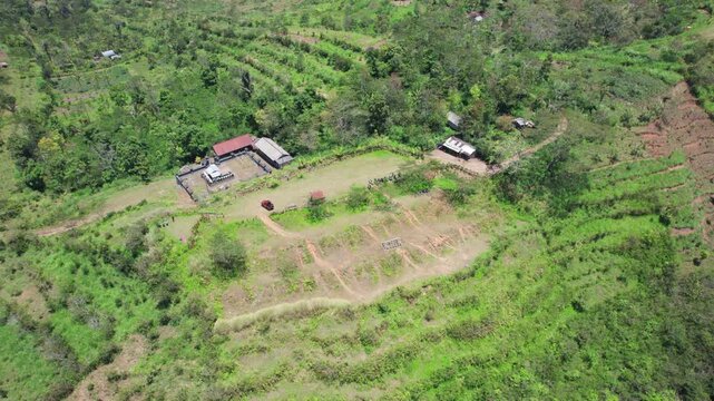 Aerial view of Bukit Cemara with lush green hills, small structures, and dirt paths in the rural landscape of Bebandem, Bali, Indonesia.