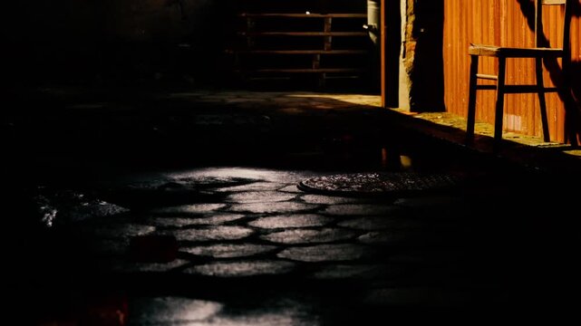 Moonlight dances on slick cobblestones, reflecting soft glimmers as shadows stretch across a serene alley. A wooden chair leans against a nearby wall, suggesting a resting moment.