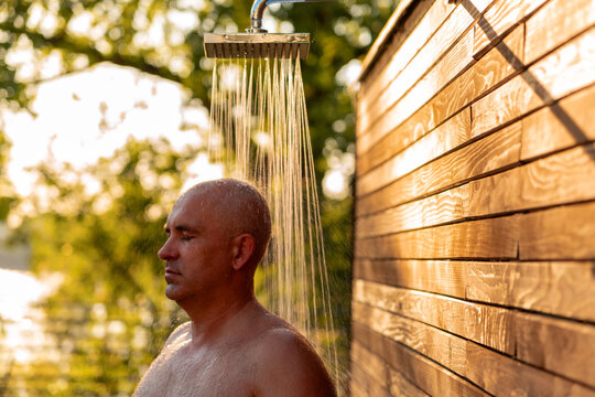 Man taking refreshing outdoor shower at sunset. Concept of relaxation and wellness