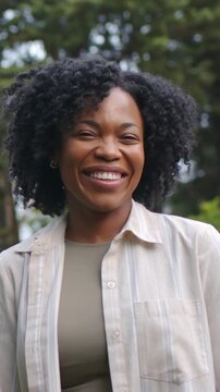 Vertical video: Smiling woman in striped shirt turning, laughing as camera tightens near pines