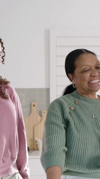 Vertical video: Seeing clip, gran in green top showing maroon phone to family, smiling in kitchen