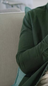 Vertical video: Settling man shifting arm, torso on sofa, showing smartwatch and shirt, copy space