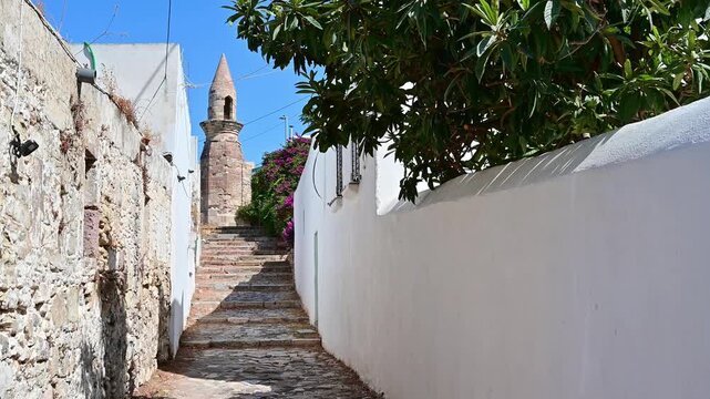 Handheld video clip capturing the ancient stone minaret and a picturesque narrow street lined with stone walls in the historic center of Kos city, Greece.