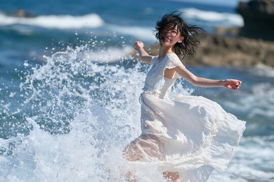 海辺で笑顔の日本人女性が水しぶき浴びてはしゃぐ夏