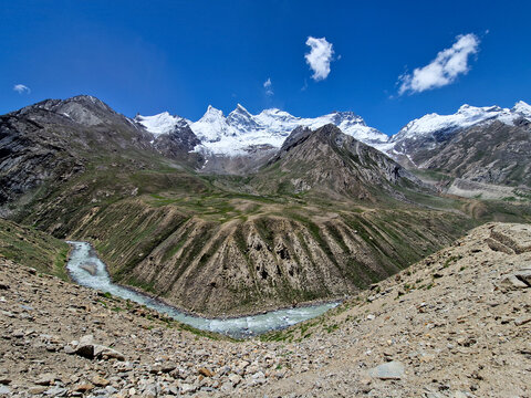 View of the Penzi La road winding through the rugged mountain landscape of the Zanskar valley, featuring snow-capped peaks, a glacial river, and rocky slopes in Zanskar, Ladakh, India.
