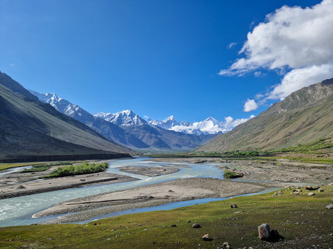 View of the winding river flowing through the Zanskar valley with snow-capped Himalayan peaks in the background under a clear blue sky in Zanskar, Ladakh, India.