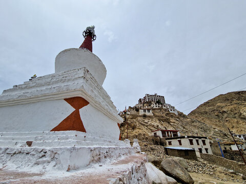 View of the white stupa at Chemrey Gompa with monastery buildings perched on the rocky hillside in Chemrey, Ladakh, India.