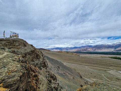 View of Matho Gompa with prayer flags on a rocky ridge overlooking the arid landscape and distant snow-capped mountains, Matho, Ladakh, India.