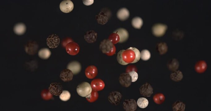 Mixed peppercorns falling on black background in slow motion 1000 fps