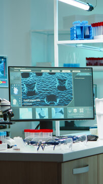 Empty laboratory workstation with a microscope, sample tubes, safety glasses and a computer displaying double-stranded DNA for molecular biology research, scientific analysis and laboratory testing.