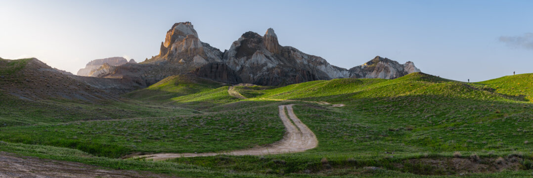 View of the Airakty mountains rising above green rolling hills and a winding dirt path in the desert landscape of Shetpe, Mangystau Region, Kazakhstan.