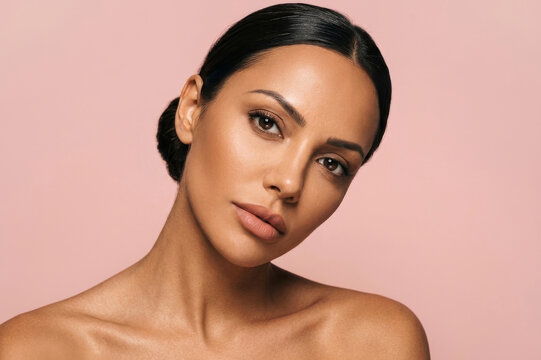 Close-up portrait of a gorgeous young woman with natural makeup posing against a pink background.