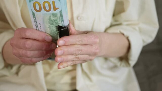 Woman's hands clipping stack of hundred dollar bills together. Unrecognizable person in a light-colored shirt securing a large wad of one-hundred-dollar bills with a binder clip, representing savings