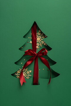 Festive Christmas cutout tree with red satin ribbon bow and golden snowflake decorations for New Year on vertical background