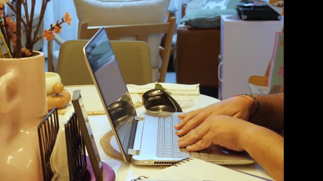 Close-up of hands typing on a laptop keyboard while using a computer mouse during a remote work session. The scene represents digital productivity, computer work, technology, online employment, and mo