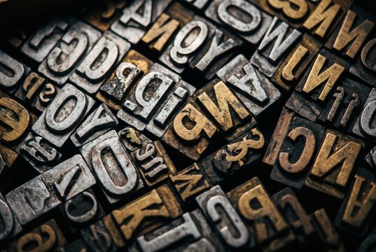Full frame of scattered vintage metal and brass letterpress type blocks, mirrored letters in warm low light