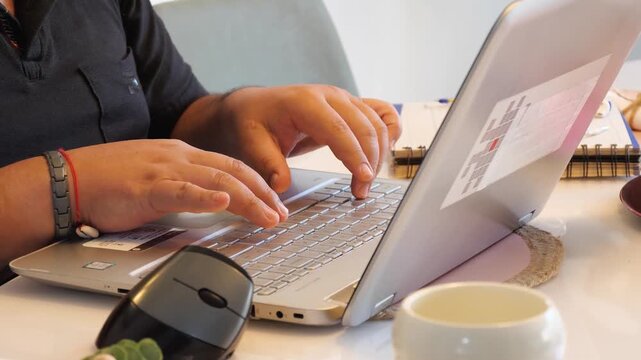 Close-up of hands typing on a laptop keyboard while using a computer mouse during a remote work session. The scene represents digital productivity, computer work, technology, online employment, and mo