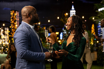 Happy guests chat over sparkling wine at a festive evening event, sharing greetings and lively conversation during an elegant nighttime social gathering. © DC Studio