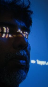 Vertical shot of middle aged South Asian cybersecurity analyst examining digital code projected on face in close up. Clip suitable for technology campaigns and IT data privacy advertisements