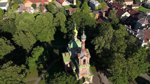 Aerial view of the Orthodox Church of the Holy Trinity surrounded by lush green trees and historic rooftops in Kuldiga, Kuldiga Municipality, Latvia.
