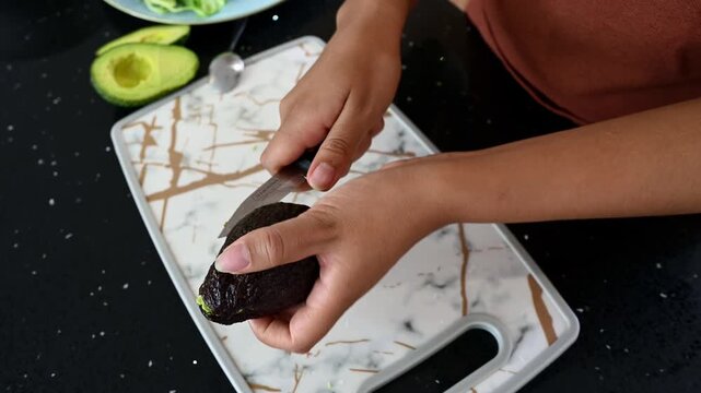 Woman's hands cutting a ripe avocado in half