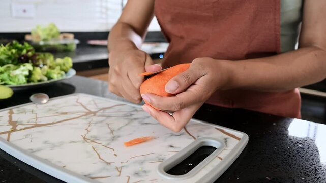 Woman peeling a fresh carrot in the kitchen