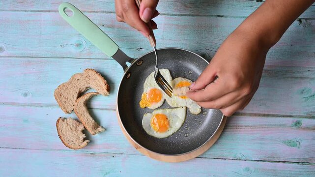 Person eating fried quail eggs with bread from a pan