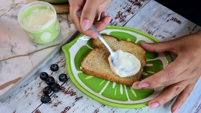Person spreading cream cheese on toast for breakfast