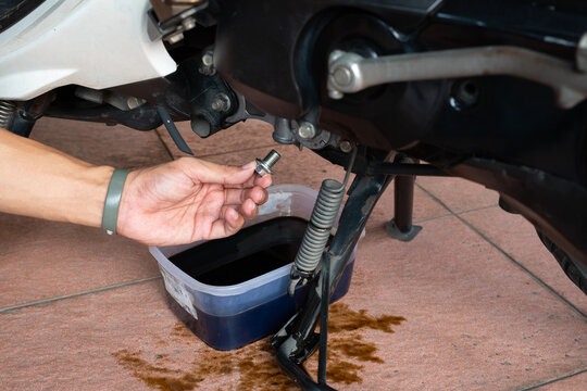 Mechanic holding oil drain plug bolt during motorcycle engine oil change service at home garage.