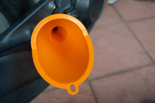 Yellow plastic funnel inserted into motorcycle engine to pour oil during service maintenance.