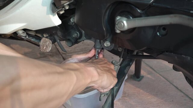 Mechanic changing engine oil on a scooter motorcycle using a socket wrench.