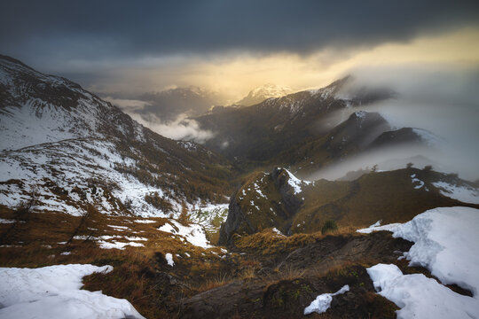 View of Passo Giau in the Dolomites with snow-covered slopes, golden autumn vegetation, and dramatic clouds at sunset in Colle Santa Lucia, Veneto, Italy.