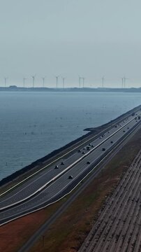 Aerial view of Windpark Fryslan with wind turbines along the Afsluitdijk causeway and highway traffic in Breezanddijk, Friesland, Netherlands.