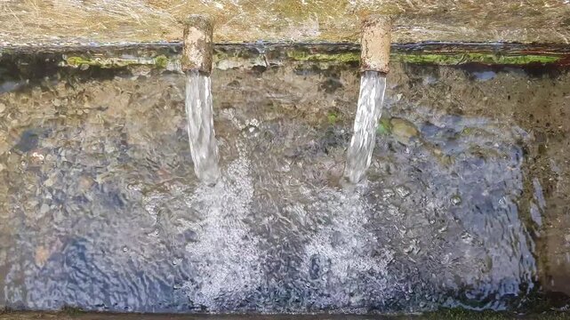 A top-down view shows two metal spouts pouring spring water at a traditional spring box catchment