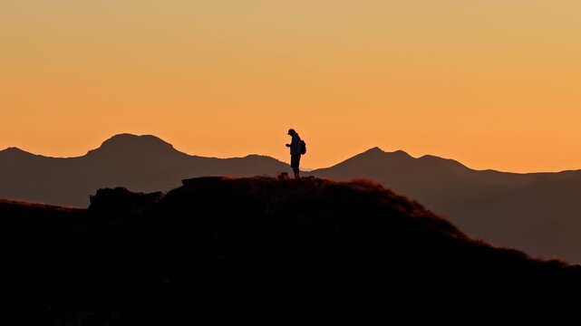 Aerial view of a person standing on the ridge of Col d'Aubisque at sunset with mountain silhouettes in the background in Beost, Nouvelle-Aquitaine, France.