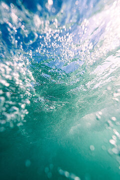 View of a breaking wave with swirling bubbles and sunlight filtering through the water surface in the United Kingdom.