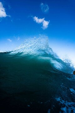 View of a powerful ocean wave breaking with sea spray against a bright blue sky in the United Kingdom.