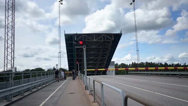 Street scene with an open bridge and traffic light under cloudy sky. People waiting in front of the barrier, G&ouml;ta Canal, V&auml;nersborg, V&auml;nern See, V&auml;stra G&ouml;talands l&auml;n, Sweden