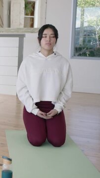 Vertical video: After meditating she kneeling on home mat turning left smiling with bottle hoodie