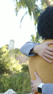 Vertical video: Hugging two adults greeting in backyard, mustard sweater and white watch visible