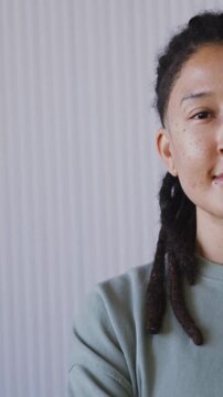Vertical video: Smiling person with dreads softening by ribbed wall in green sweater, copy space
