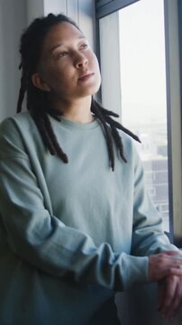 Vertical video: Glancing at camera, person in teal sweatshirt leaning on window ledge, smiling