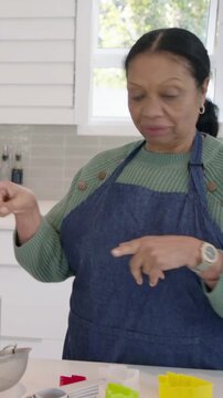 Vertical video: Hearing offframe voice, senior cook in denim apron lifting mint canister at counter